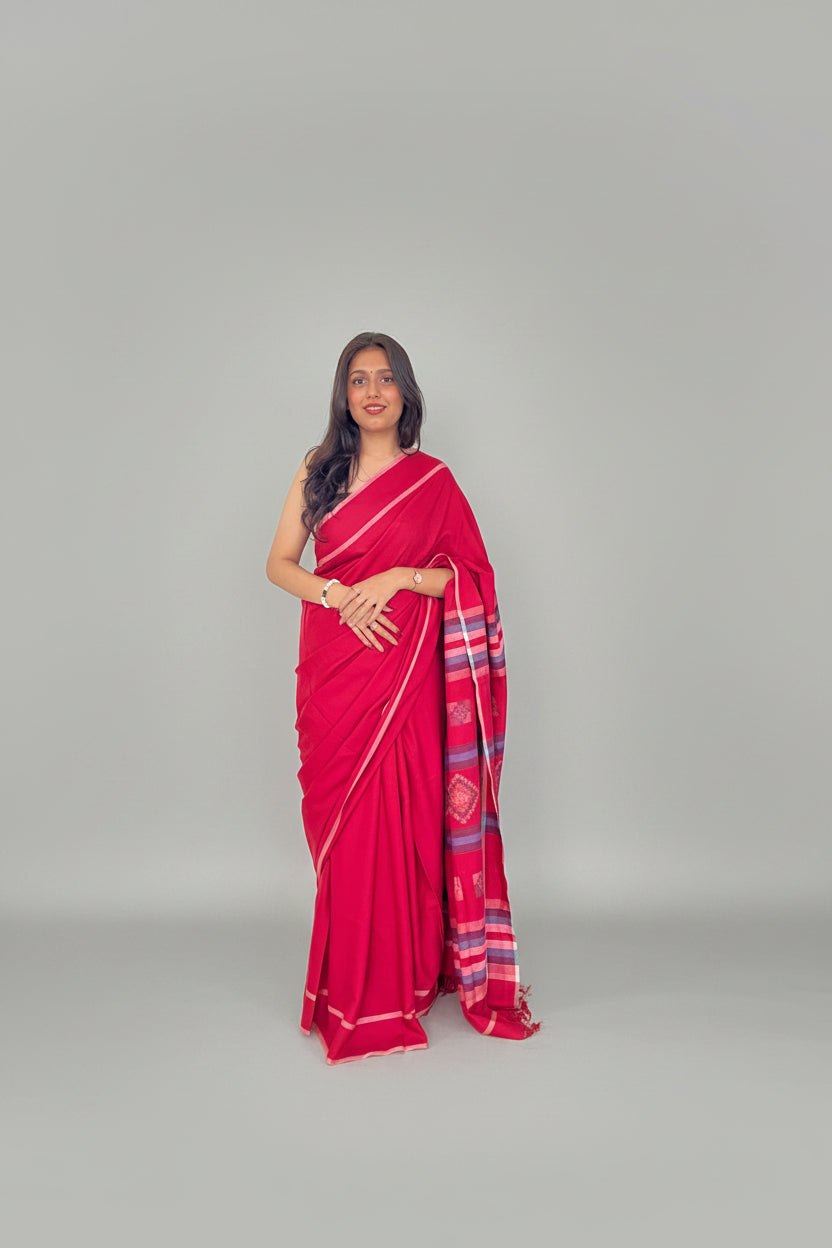 Woman wearing a pinkish-red handwoven saree with striped border and matching blouse